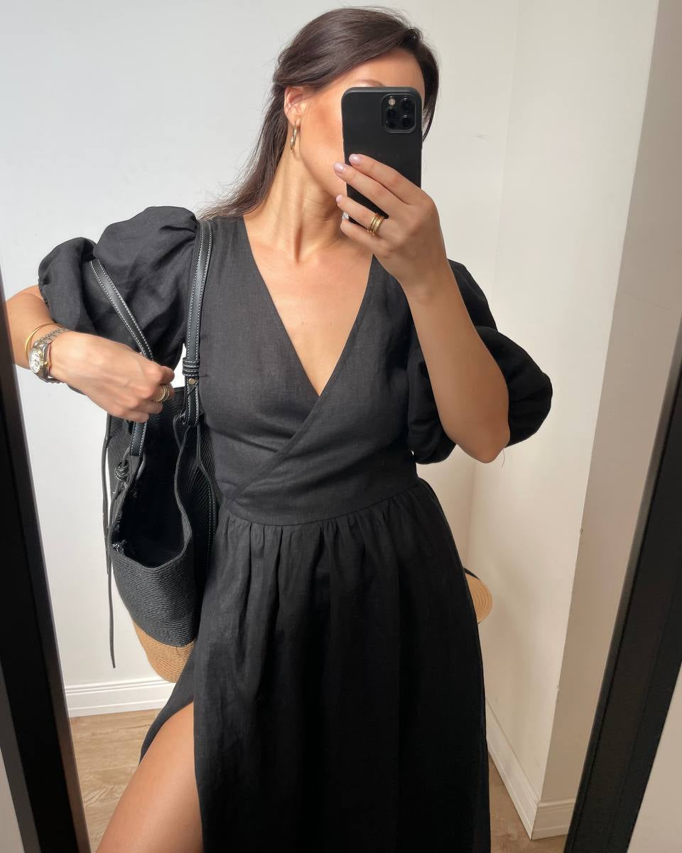 A woman takes a mirror selfie wearing a black midi wrap dress with puffed sleeves.