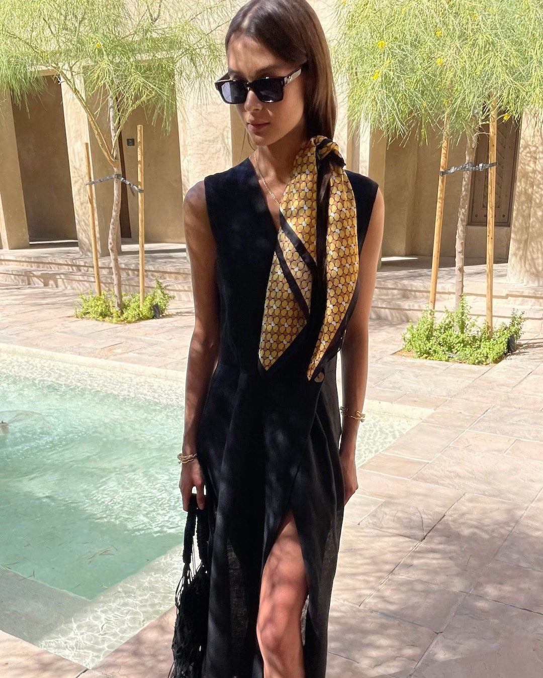 Woman in a black dress with a leopard print scarf by a poolside.