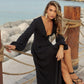 Woman in a black dress sitting by a waterfront with a wooden post and rope.
