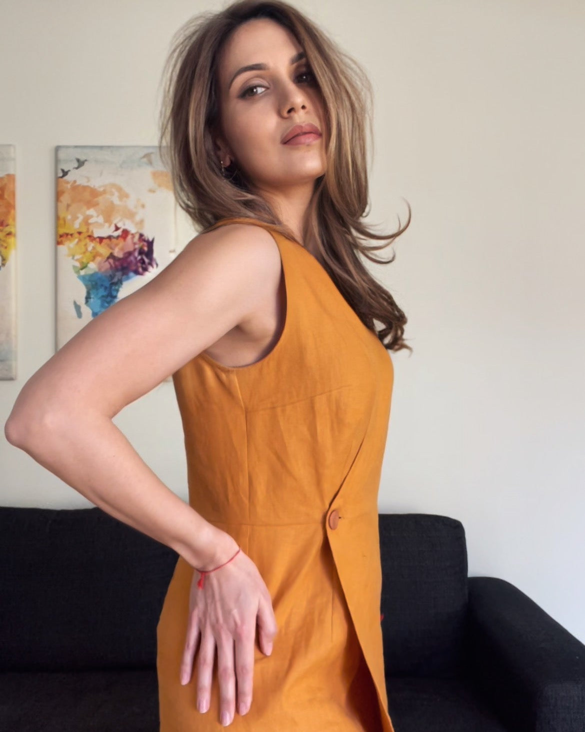 Woman in a mustard yellow dress standing in a room with a couch and colorful abstract painting.