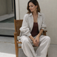 Woman sitting on a wooden chair wearing a natural linen shirt trousers set  in a minimalistic setting.
