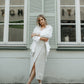 Woman in a white outfit standing in front of a building with large windows.