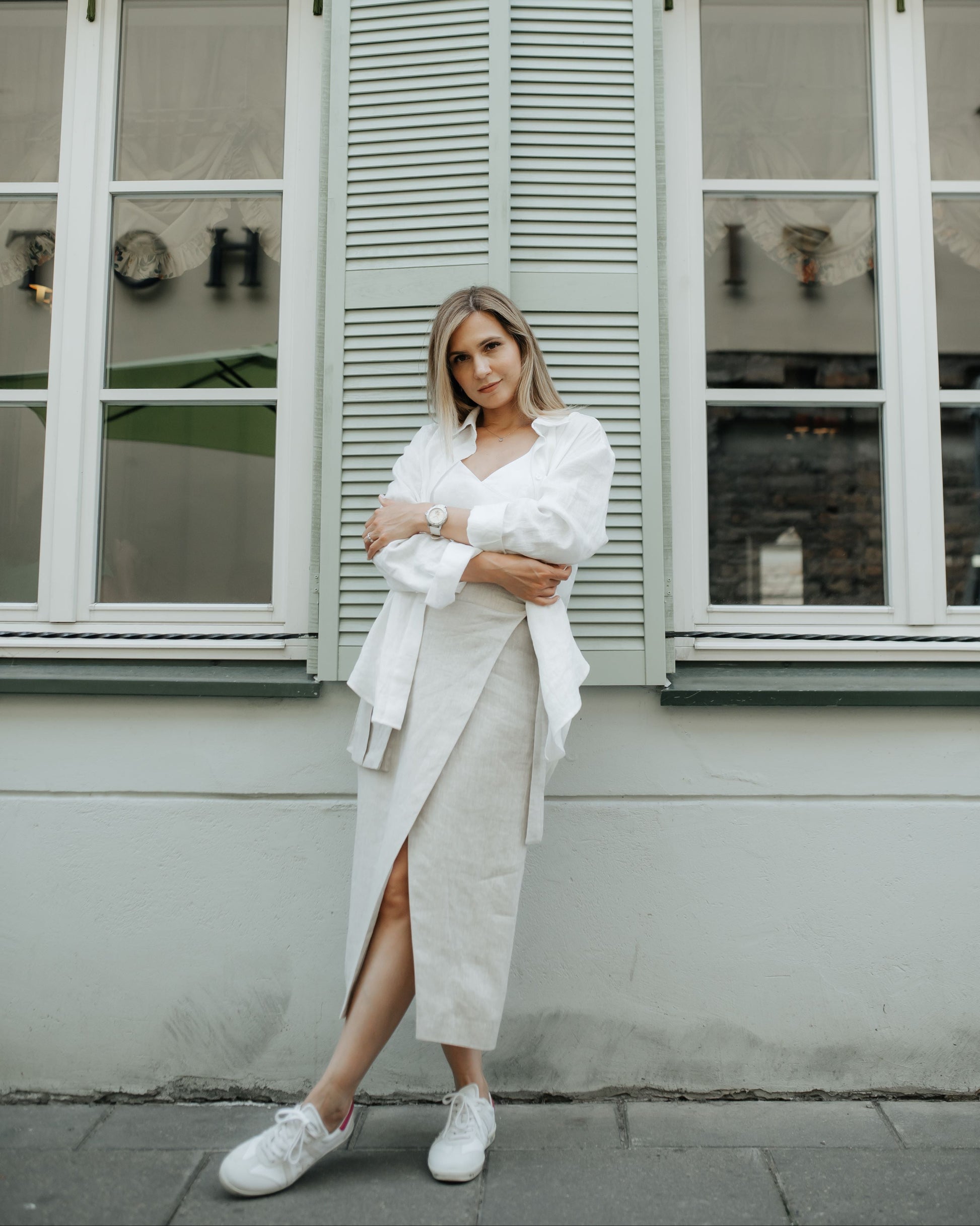 Woman in a white outfit standing in front of a building with large windows.