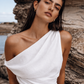 Close-up of a woman wearing a white one shoulder linen dress with a softly draped neckline and fitted waist.