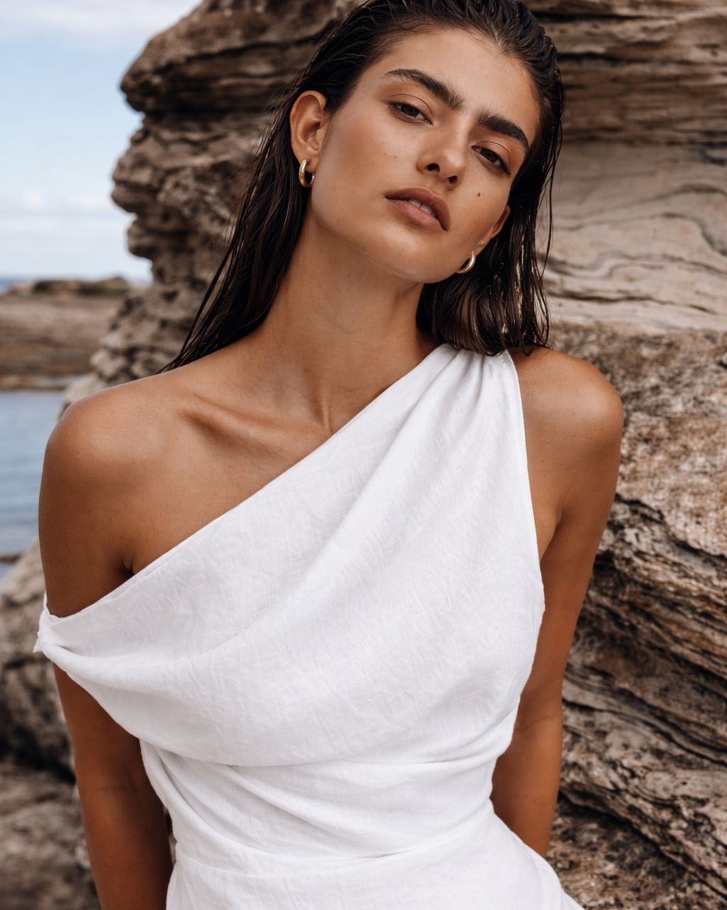 Close-up of a woman wearing a white one shoulder linen dress with a softly draped neckline and fitted waist.