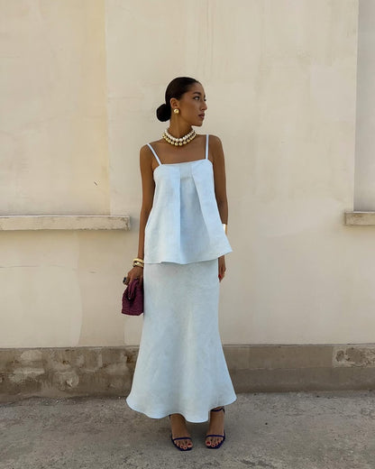 Woman in a light blue dress standing against a beige wall.