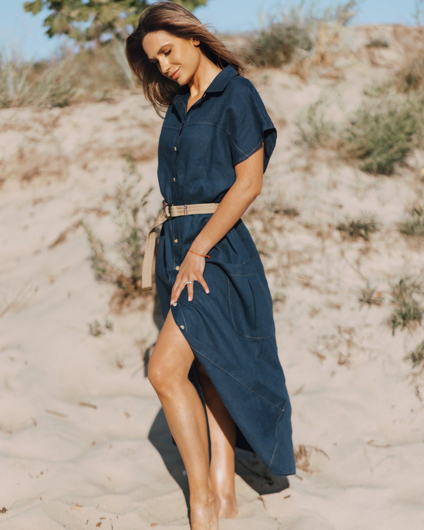 Woman in a navy dress standing on sandy terrain with sparse vegetation.