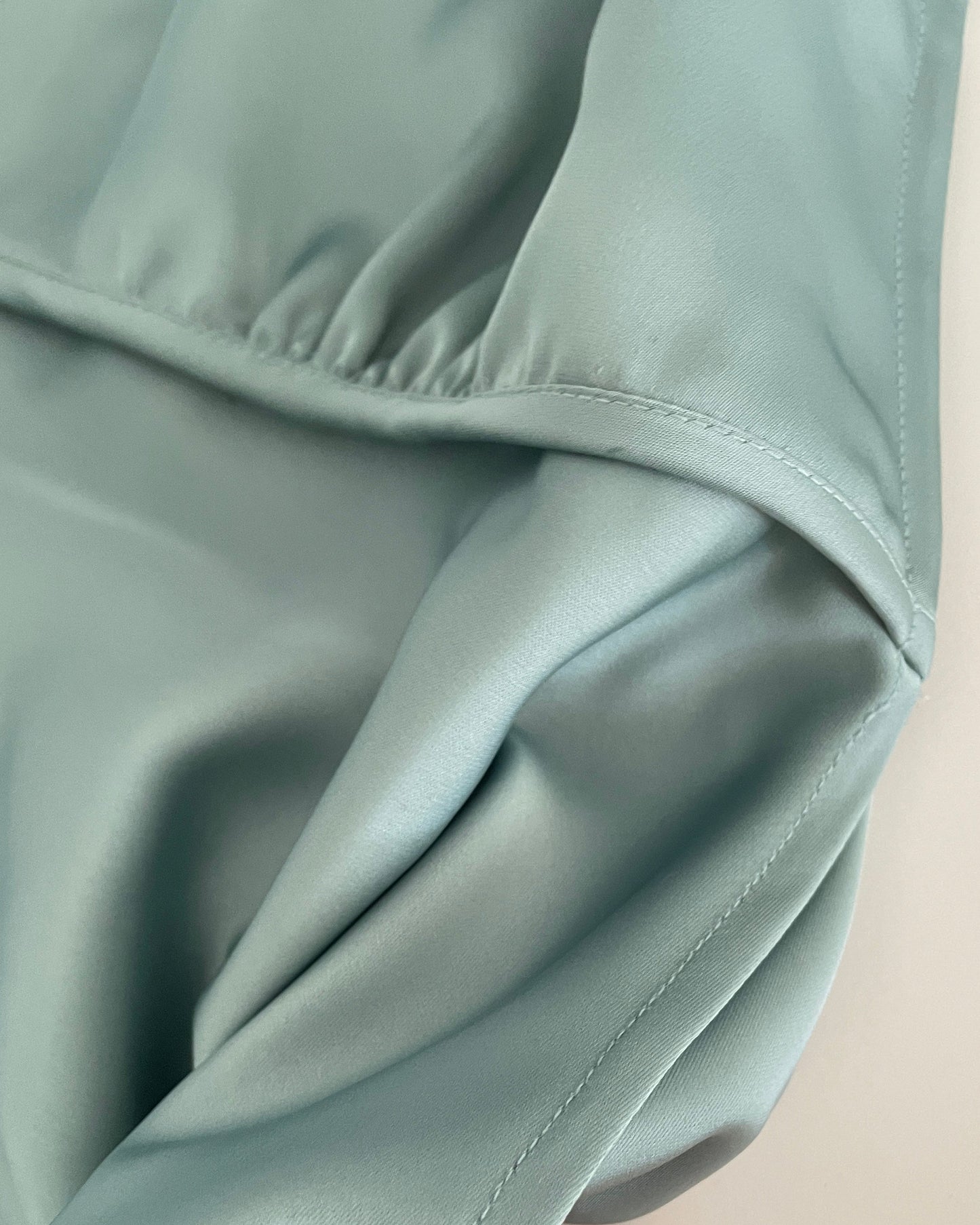 Close-up of a light green fabric with a hand holding it, on a neutral background.