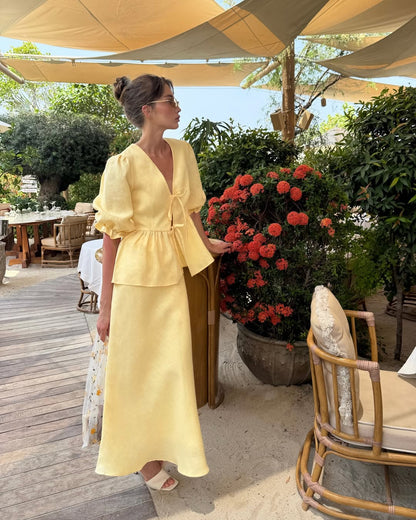 Woman wearing a butter yellow linen tie front top and bias-cut midi skirt set.