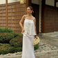 A woman wearing a white sleeveless top with thin straps and maxi skirt .