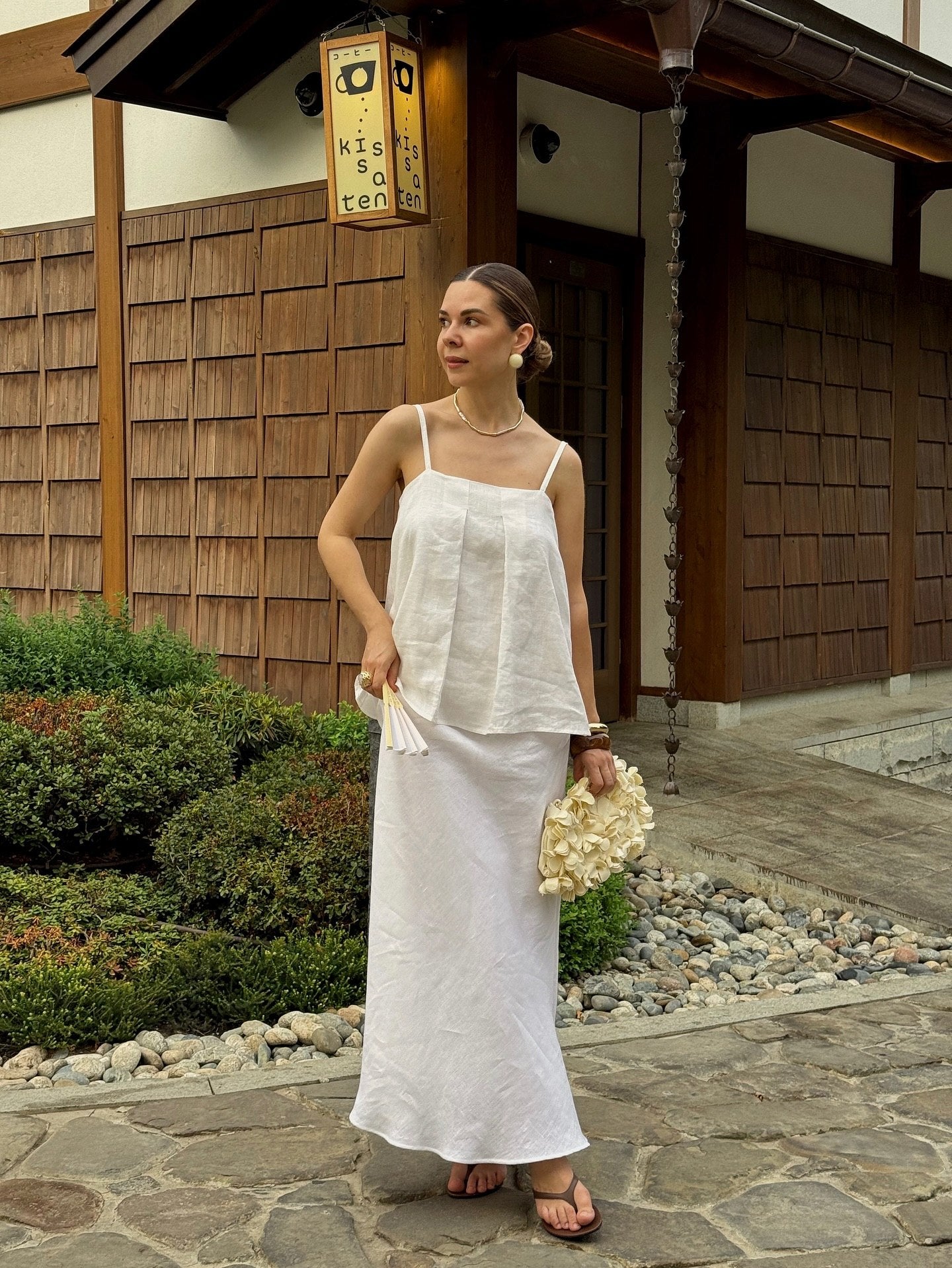 A woman wearing a white sleeveless top with thin straps and maxi skirt .