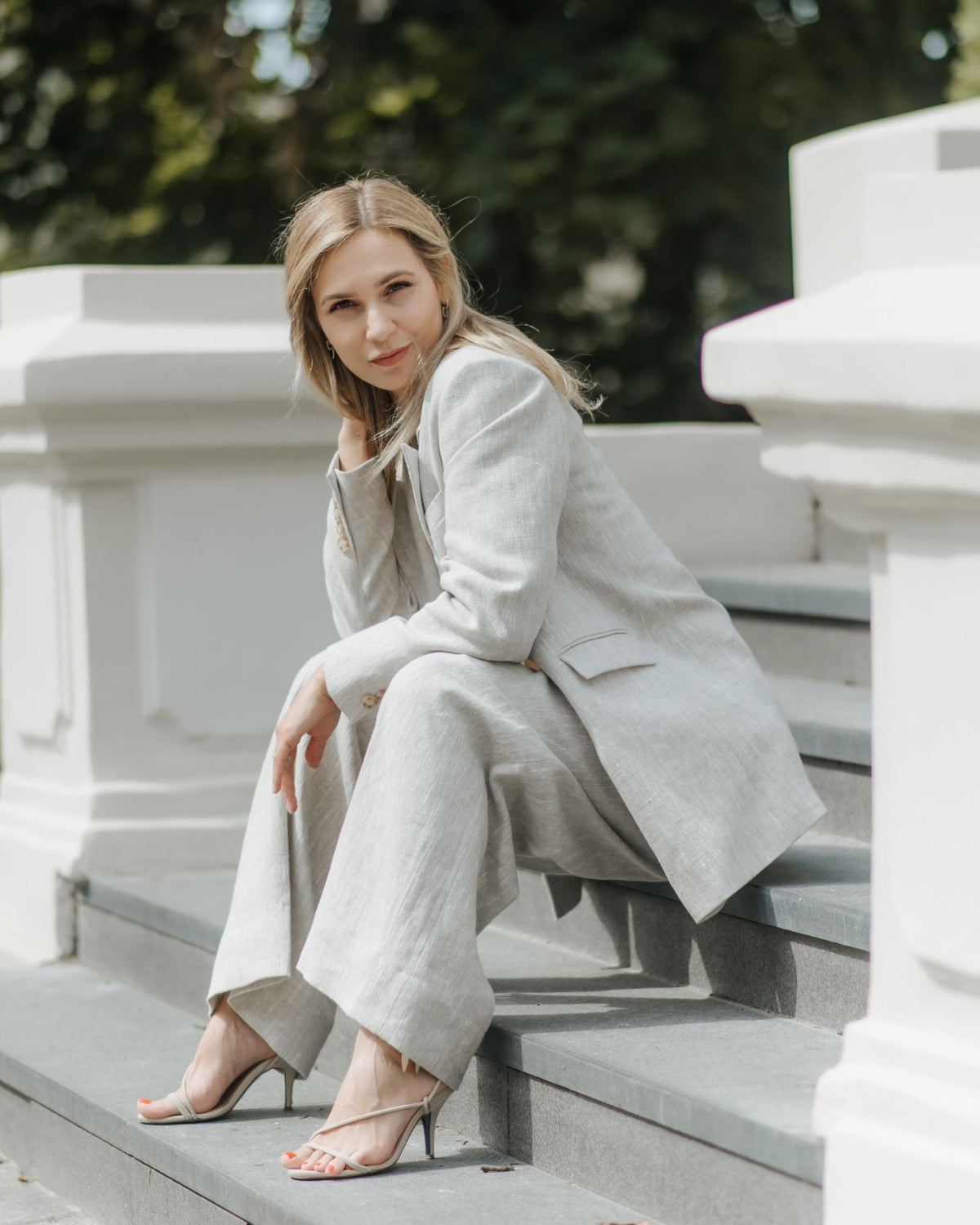 Woman seated on outdoor steps wearing beige wide-leg linen trousers with a matching linen blazer