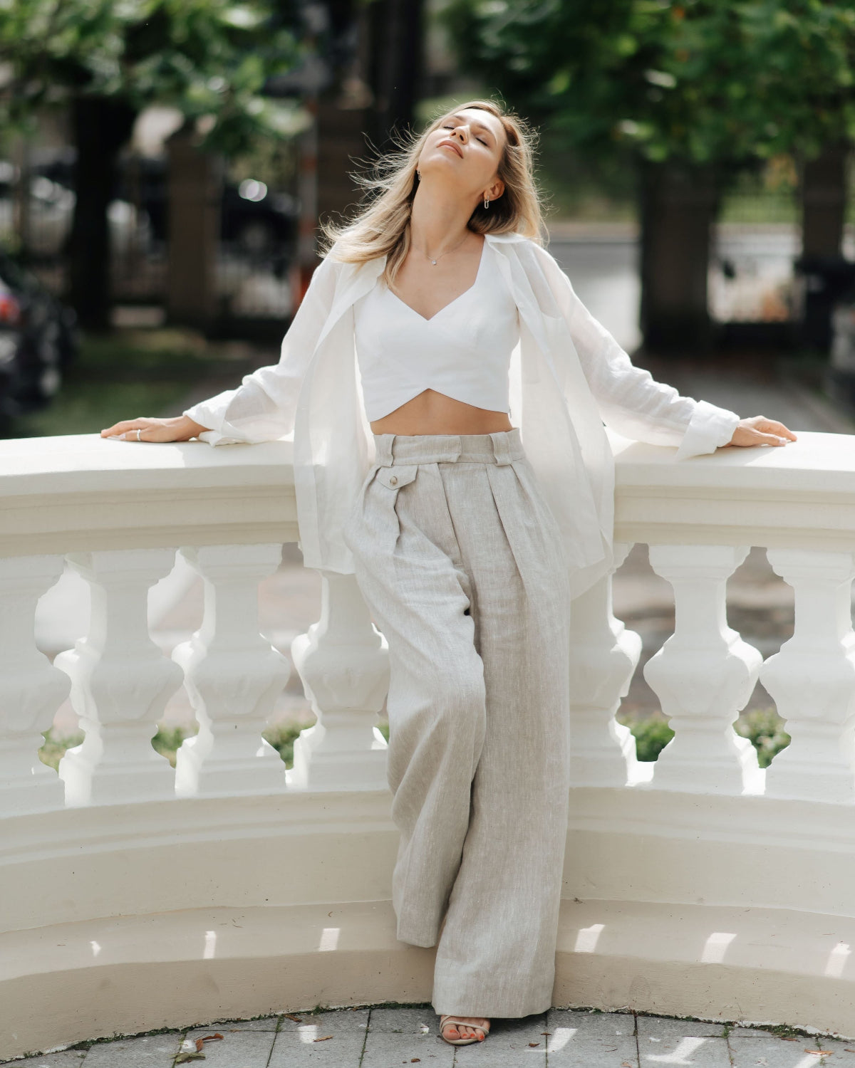 Woman wearing beige wide-leg linen trousers with a high waist and front pleats, shown in full view