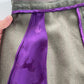 A close-up of a green textured garment with a prominent purple silk panel featuring a repeating dark horse pattern, held by a hand on the left.