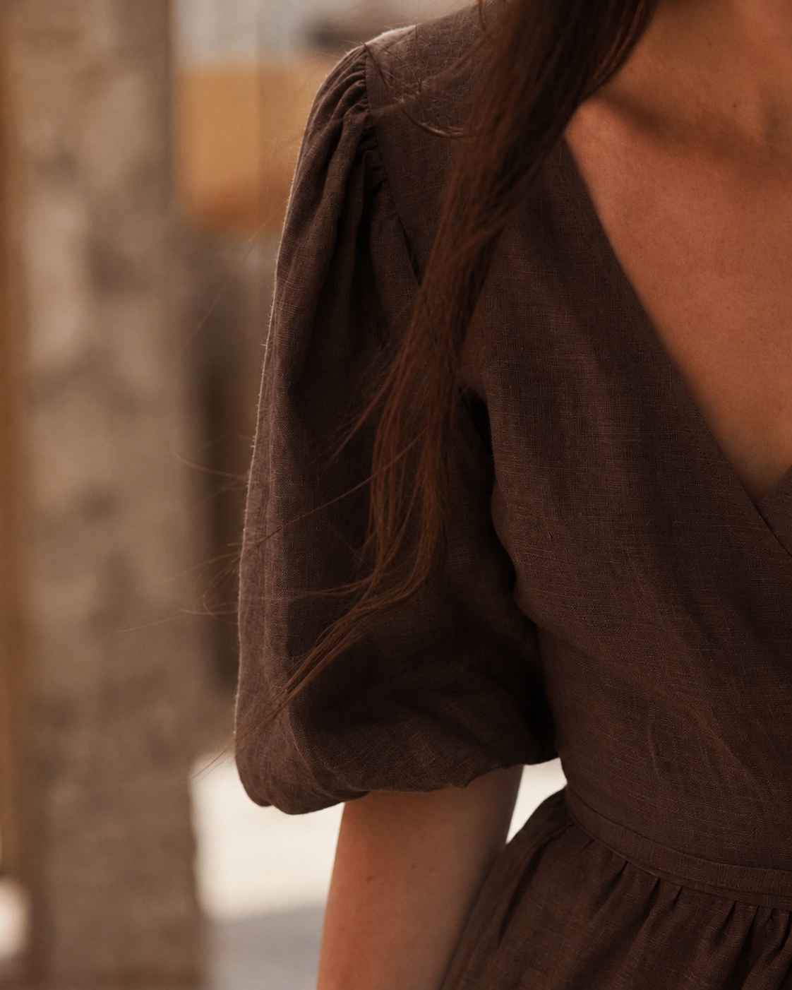 Close-up of a person wearing a brown linen dress with a deep V-neckline and voluminous puff sleeves.