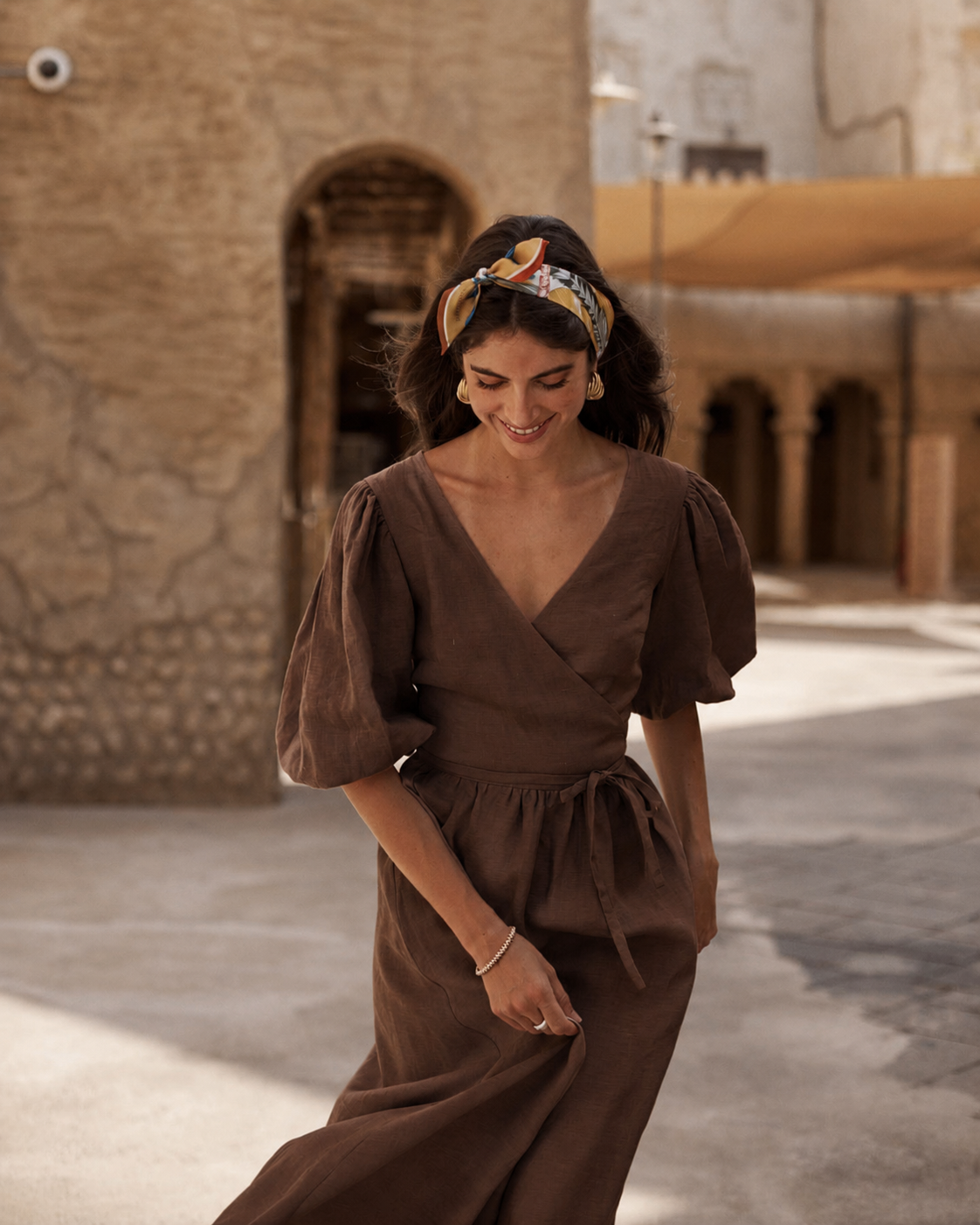 A woman wearing a brown wrap-style midi dress with puff sleeves and a waist tie, walking outdoors.