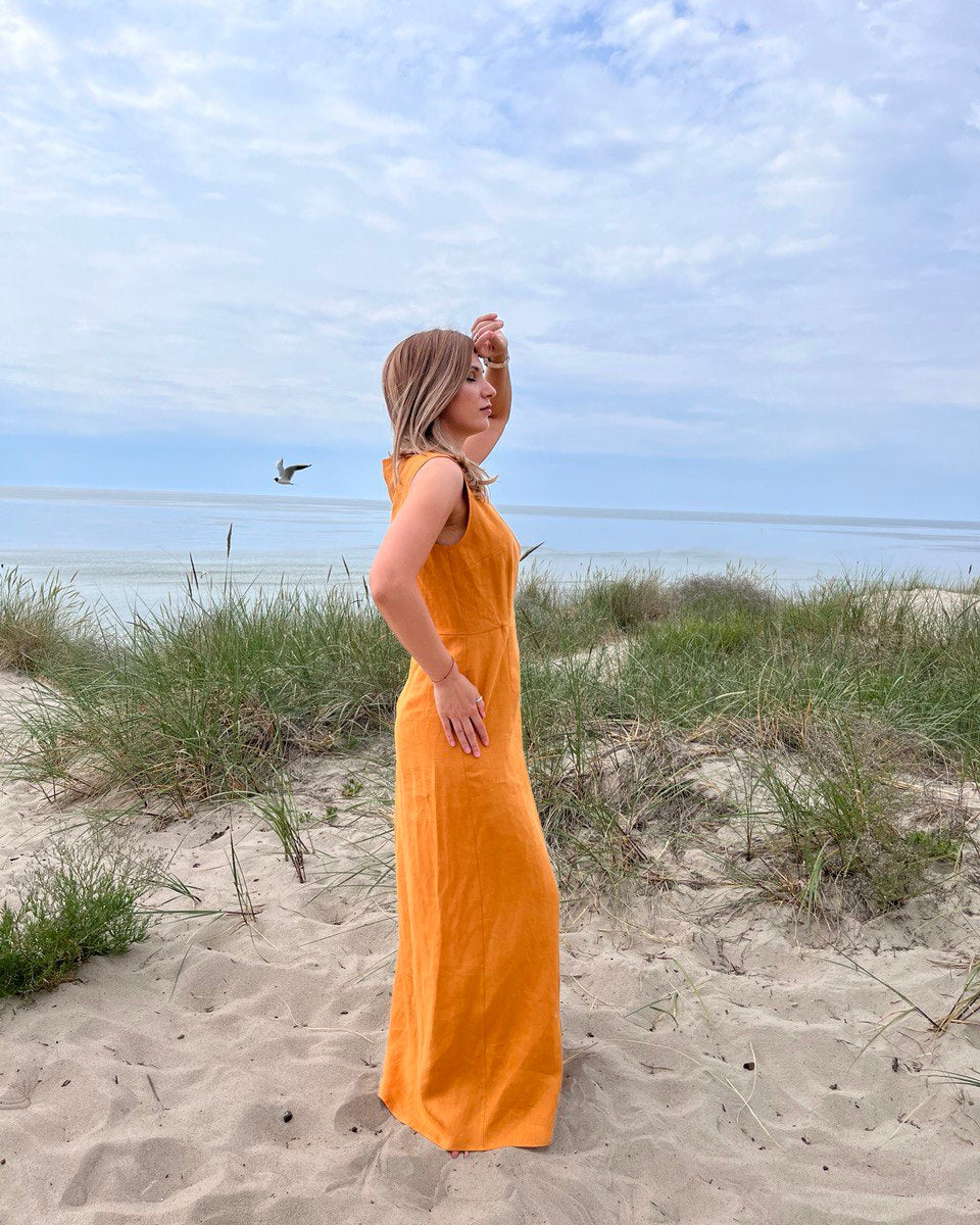 Woman in a yellow dress standing on a sandy beach with grass and water in the background