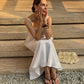 A woman wearing a white linen top and skirt  and brown sandals sits on stone steps outdoors.