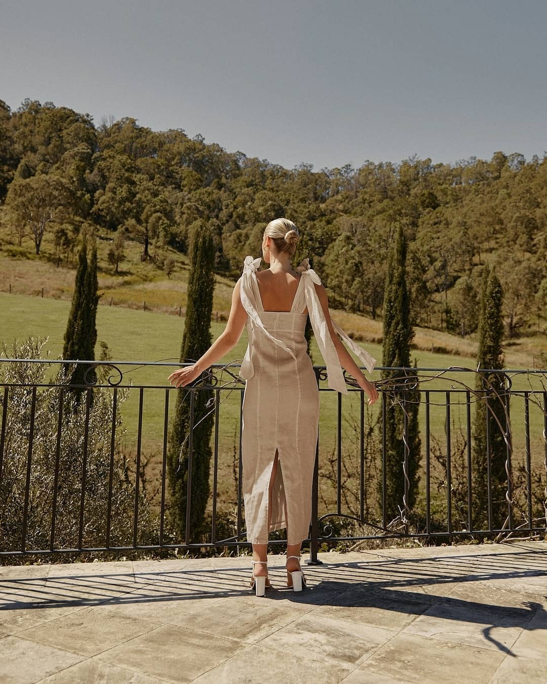 Back view of a beige linen midi dress with back slit and tie shoulder straps