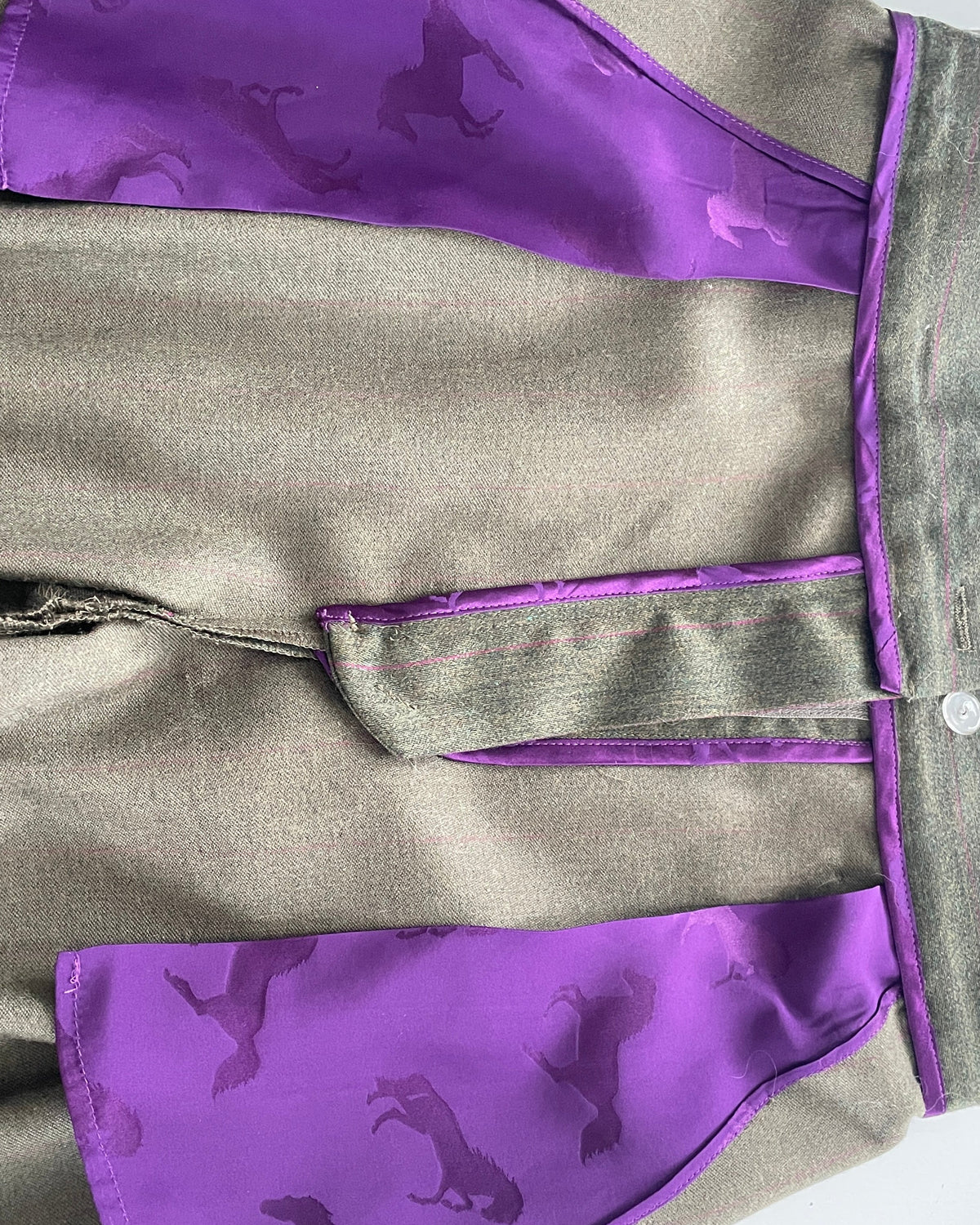 A close-up of a garment featuring a textureddark green fabric body with vibrant purple silk panels and trim, decorated with dark purple horse silhouettes.