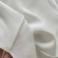 A close-up of a white silk dress inside with a hand holding the edge to show the smooth texture and fine stitching.