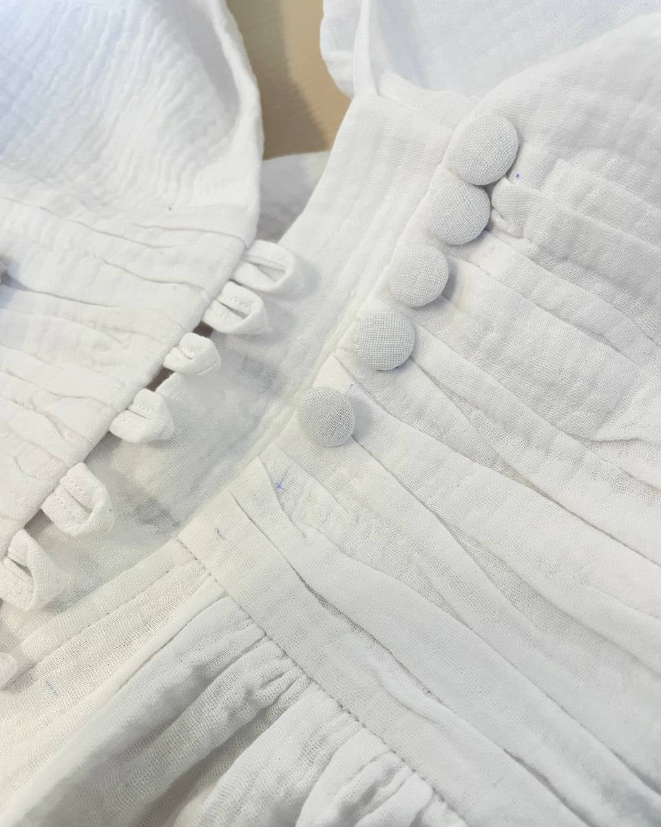 Close-up of the cream white muslin wedding dress showing the textured cotton fabric, draped waist and fabric-covered buttons.