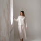 Full length back view of a woman walking indoors in an ivory silk midi dress with long flowing skirt