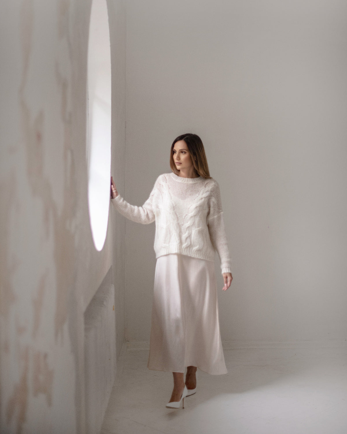Full length back view of a woman walking indoors in an ivory silk midi dress with long flowing skirt
