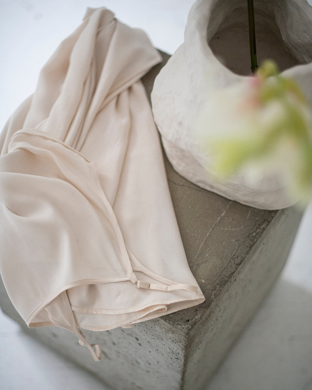 Ivory silk satin dress draped over a stone pedestal beside a white vase with flowers