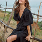 Woman in a black wrap dress sitting on a wooden fence with a scenic background