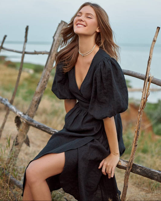 Woman in a black wrap dress sitting on a wooden fence with a scenic background