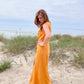 Mustard sleeveless linen wrap maxi dress on a sandy beach.