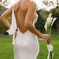 Woman holding white calla lilies while wearing an ivory open back silk maxi dress.