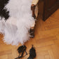 White silk chiffon bridal cape with natural ostrich feather trim draped over a vintage chair, with black feather-trimmed high-heeled sandals on the wooden parquet floor.
