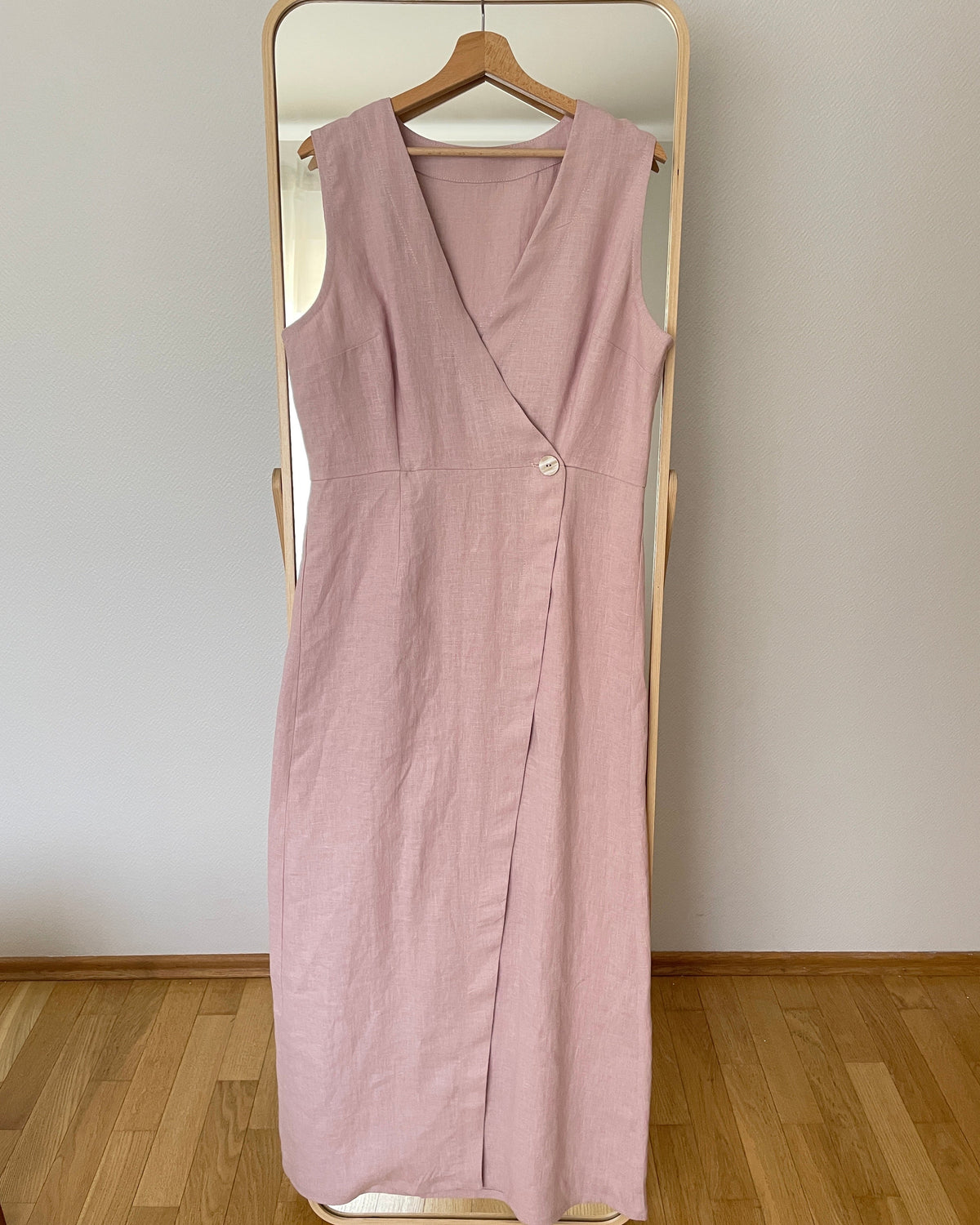 Pink dress with a V-neck, defined waist and button fastening, shown hanging on a wooden hanger.