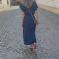 A woman in a dark blue long linen dress with buttons walks through the old town