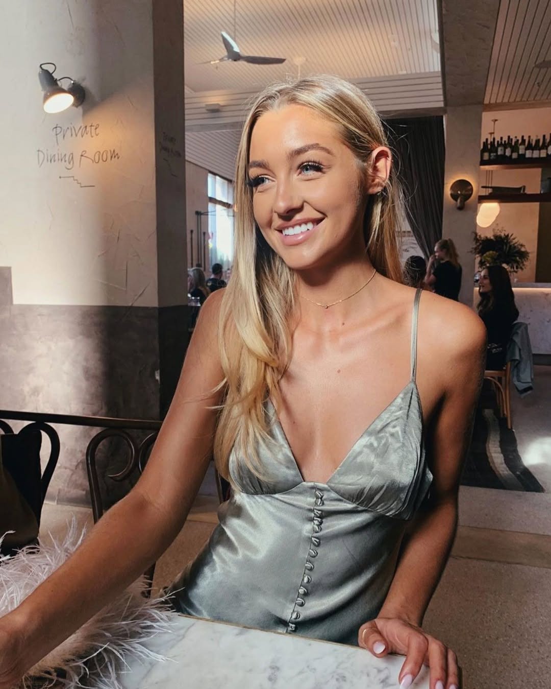 Woman sitting at a café wearing a sage silk slip dress with thin straps