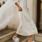 Close view of a woman walking down stone steps in a white wedding dress, with a sheer silk chiffon bridal cape flowing behind her and white feather-trimmed heels.