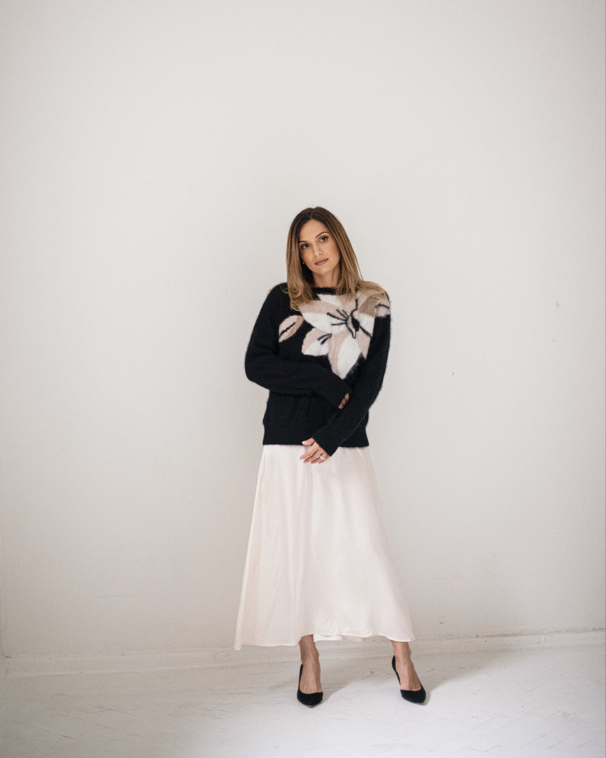 Woman wearing an ivory silk midi dress layered with a black floral sweater and black heels