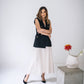 Woman in an ivory silk midi dress layered with a long black vest and worn with black heels