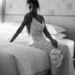 Bride wearing an ivory backless silk maxi dress sitting on a bed holding white calla lilies.