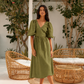 A woman wearing an moss  green midi dress with puff sleeves, a V-neckline, and a tie waist. 