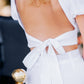 Close-up of the white backless linen top, showing the open back and long adjustable bow ties at the waist.