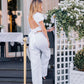 Woman wearing a white backless linen top with a large bow and white wide-leg trousers, walking into a city restaurant.