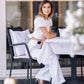 Woman wearing a white linen crop top with puff sleeves and matching wide-leg trousers, seated at an elegant outdoor city cafe.