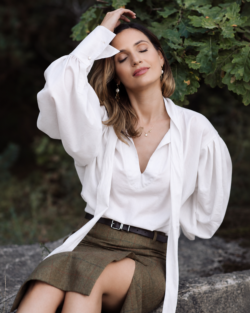 Woman wearing a white ascot tie-neck blouse with shoulder draping, voluminous sleeves and long structured cuffs.