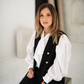 White tie-neck blouse with voluminous sleeves layered under a black tailored vest.