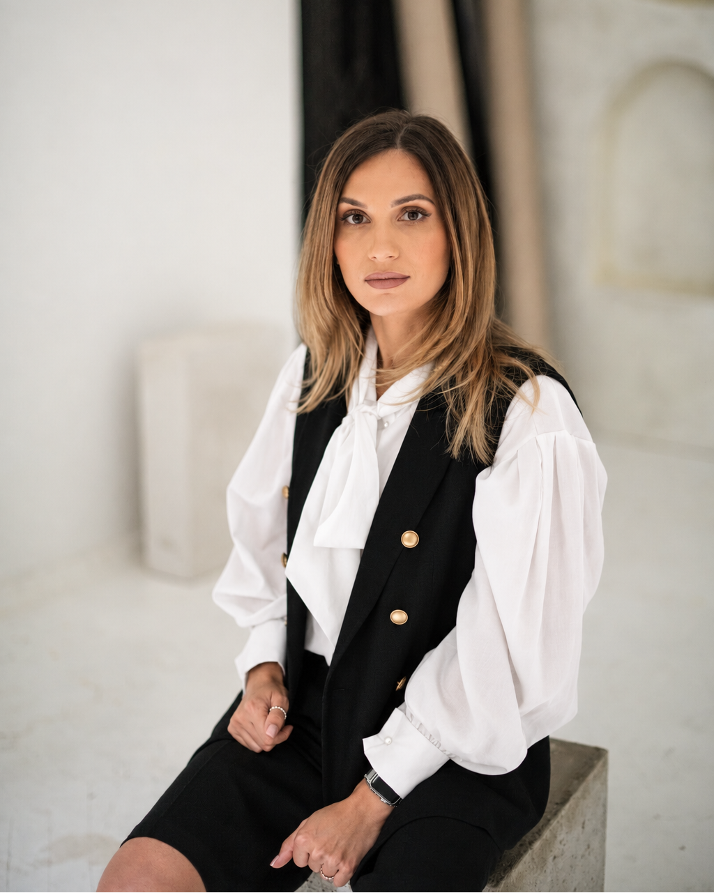White tie-neck blouse with voluminous sleeves layered under a black tailored vest.