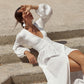 Woman wearing a white cotton muslin boho wedding dress with a deep V-neck, draped waist and fabric-covered front buttons, sitting on stone steps.