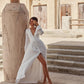 Woman wearing a white long sleeve boho wedding dress with a deep V-neck and button front, shown full length in a sunlit desert setting.